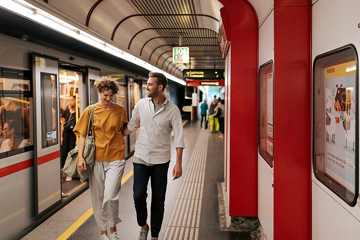Mann und Frau gehen nach dem Aussteigen umschlungen an einem Wiener U-Bahn Gleis entlang