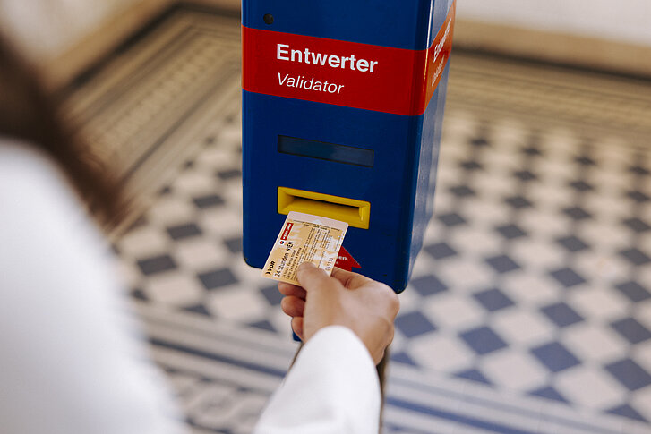 Frau in U-Bahnstation hält Wiener Linien Ticket aus Papier in Entwerter